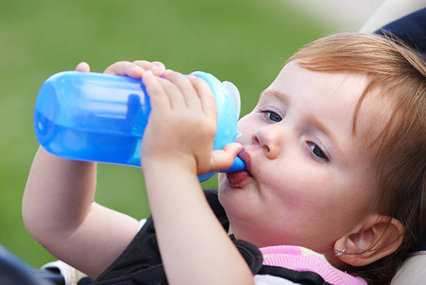 Two years old girl child drinking from blue plastic bottle